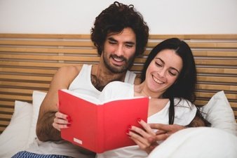 couple-smiling-while-reading-a-book-in-bed_23-2147595879
